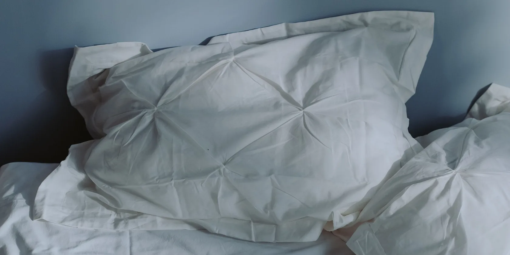 Oreillers blancs froissés dans la pénombre bleutée d'une chambre
